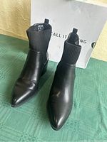 Pair of black ankle boots with pointed toes, ribbed fabric cuffs, size label visible inside.