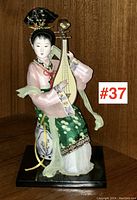 Front view of porcelain figurine showing full costume, face, headdress, and musical instrument.