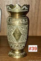 Front view of brass vase showing diamond shaped and floral engraved patterns, scalloped rim, and flared base.