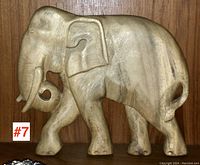 Clear side view of entire carved wood elephant plaque showing shape and size against wood background.