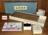 Chinese Go game set including wooden board with grid, black and white playing stones in boxes, original blue fabric-covered storage box with Chinese label, and instruction booklet