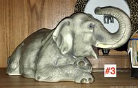 Side view of ceramic elephant showing body and face with trunk raised.