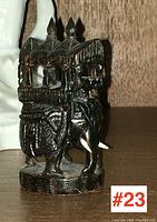 Front angled view of the dark wooden carved elephant with a carved howdah on its back, showing tusks and detailed ornamentation.