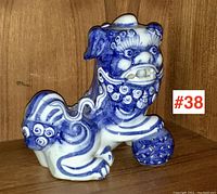 Front left three-quarter view of foo dog kneeling with ball under right paw