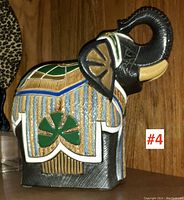 Front and left side view of black pottery elephant figure with raised trunk and multicolored decoration leaning against a wood background.