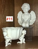 Full view of the putti jardiniere with two putti figures supporting the bowl and the ceramic angel figure beside it.