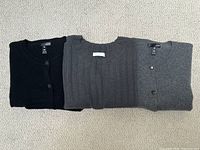 Three folded cashmere sweaters: black cardigan, charcoal ribbed T-shirt, light grey cardigan