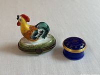 Image showing a Limoges porcelain rooster trinket box and a Halcyon blue enamel pill box side-by-side on white surface.