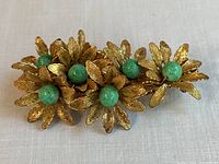 Top view of the brooch laid flat on fabric background showing six gold filigree flowers with green glass pearl centers