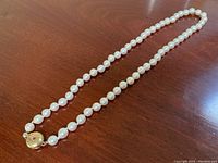 Full-length view of pearl strand with clasp on wood surface