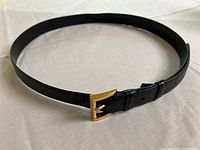 Full view of black patent leather belt laid flat showing overall shape, texture, and buckle design.