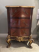 Front view showing bombe-shaped front, three drawers, brass pulls, gilt carved apron and cabriole legs