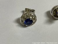 Close-up of one earring showing oval blue sapphire center and diamond halo