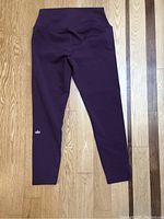 Full view of purple Alo leggings laid flat on wood floor, showing the length and color.