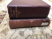 Photo showing two antique books stacked, one titled 'The New Home Encyclopedia' in maroon leather and one with a worn reddish-brown cover.