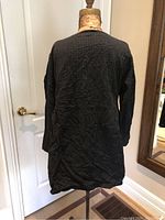 Back view of black linen textured jacket on mannequin, showing length and pattern.