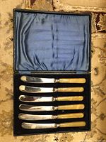 Full view of the set of eight butter cutting utensils in the silk-lined black case with blue satin interior.