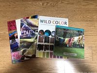 Four books stacked on a wooden floor showing covers related to tie dye and natural dyeing.