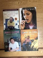 Four cookbooks arranged on wooden floor: three by Jamie Oliver and one by Nigella Lawson