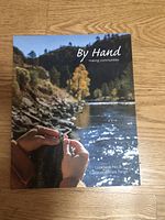 Craft book 'By Hand' with cover showing hands knitting near a river scene outdoors