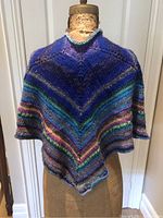 Front view of multicoloured hand knit shawl displayed on a dress form showing V shaped striped pattern.