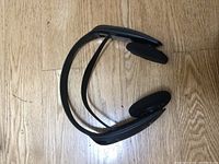 First black headphone set shown from side angle on wooden floor, showing flexible headband and foam ear pads.