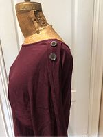 Side view showing deep purple dress fabric and two silver decorative buttons on the shoulder of the dress.
