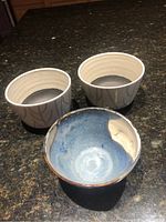 Three ceramic bowls shown together; two white with black interior and blue branch pattern, one blue and earth tone rustic bowl.