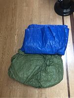 Blue and green tarps folded on a wooden floor, showing their size and color.
