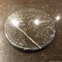 Top view of round deep green soapstone lazy Susan cheese board on a dark surface, showing natural white veins.