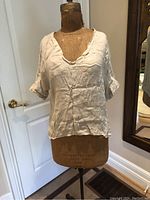 Front view of off-white linen short-sleeve blouse on a dress form showing scoop neckline and natural wrinkles in fabric.