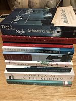 Nine trade paperback literary fiction books stacked on a wooden surface, showing spines and covers with clear titles and authors.