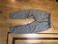 Full view of gray track pants laid on wooden floor, showing overall condition and style.