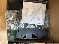 Contents inside the box: black metal mount parts, screws and bolts in plastic bags, and instruction manual labeled E26SB.