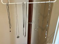 Front view of multiple silver necklaces hanging from a display rack, showing various chain styles and pendants.