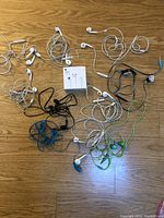 Top view of ten tangled sets of assorted wired earphones in multiple colors on wooden surface.