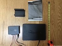 Full kit laid out showing wireless speaker, control box with wires, mounting bracket, user manual, and measuring tape for scale.