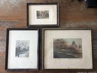 Three framed Wallace Nutting colored photographs displayed on a wooden surface, one large gold frame, two smaller wooden frames, one missing glass