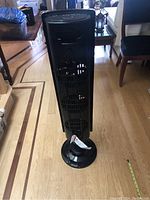 Full front view of the Westinghouse black tower fan showing the three fan vents and circular base on wooden floor.