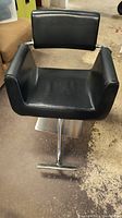 Black leather barber chair with cushioned seat, backrest, armrests, and metal base with footrest