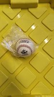 Photo of Rawlings Official League hard baseball sealed in plastic wrap on yellow plastic surface.