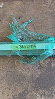 Grey window blinds wrapped in green plastic on a concrete floor, showing dimensions on label: W 38in x L 78 1/2in.