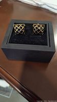 Pair of black and gold cuff links displayed in a black foam-lined box, showing front face design.