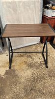 Desk with brown wood surface and black metal legs shown from front and slightly angled side view. The desk surface appears smooth and in good condition with no visible scratches or marks. The black metal frame has angled legs joined by a horizontal support bar near the bottom.