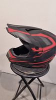 Side view of red and black motorcycle helmet without front shield placed on stool against wall.