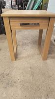 Front view of small wood table with drawer on concrete floor
