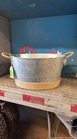 Steel metal pail wrapped with rope at the base and with rope handles on either side placed on a metal surface.