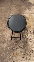Top-down view of round black faux leather stool seat and legs on concrete floor