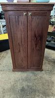 Front view of closed wood cabinet showing two doors with brass/gold knobs and wood grain finish.