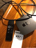 Apple TV unit with remote and cable positioned on wooden surface.